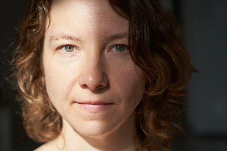 Caucasian female adult with curly hair in soft light close-up portrait.の写真素材
