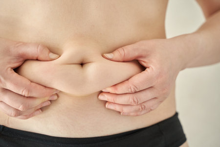 Close-up of hands pinching skin on male abdomen displaying body fat for health awareness.