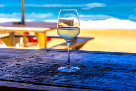 A glass of white wine on wooden table of outdoor restaurant on the beach. Sea view. Summer beach vacation. Hight quality photoの写真素材