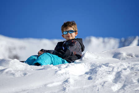 Young Boy Sitting On The Snow Mountain. Winter timeの写真素材