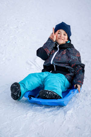 Young Boy Sitting On The Blue Sled on the Snow Mountain. Winter holidays timeの写真素材