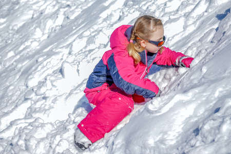 Outdoor winter portrait of little cute girl in the sunglasses and wearing ski clothes. Girl playing with snow. Stylish clothes for kids.の写真素材
