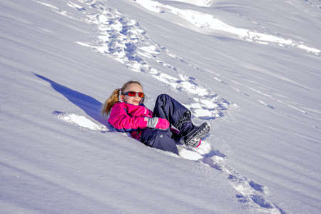 Beautiful girl wearing a pink ski jacket playing and running in a snowy winter park on Christmas dayの写真素材