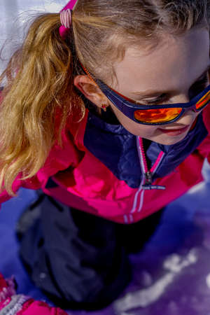 Outdoor winter portrait of little cute girl wearing sunglasses and ski clothes. Stylish clothes for kids.の写真素材