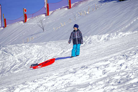 Young boy going with a sled on a winter day. Snow backgroundの写真素材