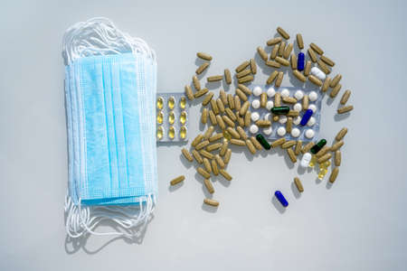 A table with several surgical masks. Assorted pharmaceutical medicine pills, tablets and capsules near the masks. High quality photoの写真素材