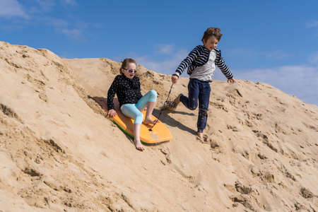brother and sister slide out of a sand on a boardの写真素材