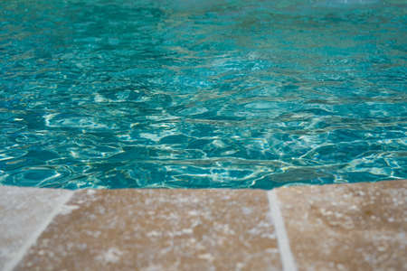 Open swimming pool edge, water and beige marble texture. Vacation, holiday. Ripple water. Water color abstract texture. Swimming pool water sun reflection background. Selective focusの写真素材