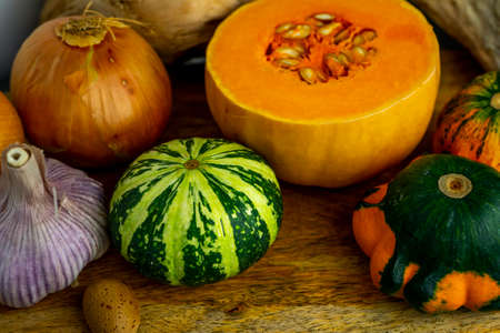 Still life with autumn vegetables and fruits on wooden background. Pumpkins, butternut, garlic, bow.