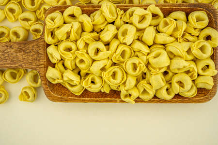 Background Italian uncooked pasta Tortellini with cheese on a wooden plate. Traditional Italian food. Selective focus. Macro close-up, copy spaceの写真素材