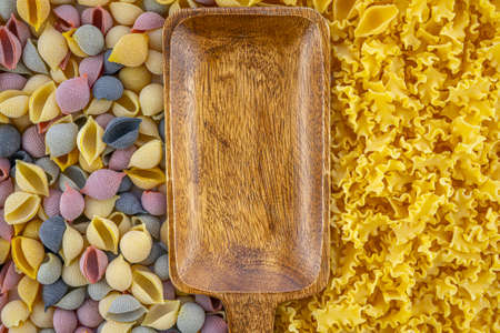 Italian uncooked colored pasta in the shaped of seashells with yellow, pink, and purple colors, wavy...