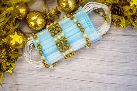 Composition with blue medical corona virus face masks and winter decoration with gold balls on blurred wood background. Merry Christmas in covid-19 pandemic. High quality photoの写真素材