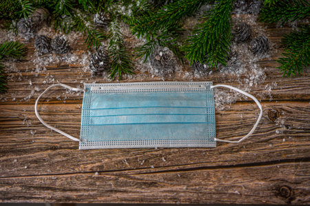 Christmas decoration background. Protective masks on wooden table. Fir tree branches and shiny gray...