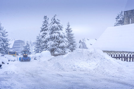 Auron, France 01.01.2021 A harvesting tractor cleans snow in a ski resort on the road in a heavy snowfall. Mountain village. High quality photoの写真素材