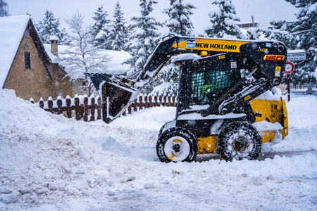 Auron, France 01.01.2021 Wheel loader machine removing snow on a ski resort. Clearing the road from...