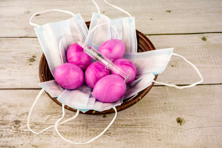 Easter traditional painted pink eggs with syringe and a protection masks in a wicker basket as...