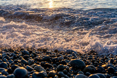 Golden pebbles on seashore in morning sun light. Sea wave on seacoast with round stones. Mediterranean sea coast. High quality photoの写真素材