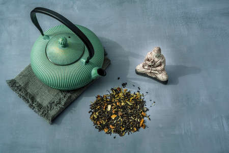 Dried Organic Green Tea Leaves with herbs and fruits on gray Background. Composition with Iron teapot, linen cloth and Buddha statue. Asian tradition tea ceremony. High quality photoの写真素材