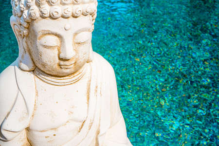 White Buddha statue on azure water background. Founder of Buddhism. Close up.の写真素材