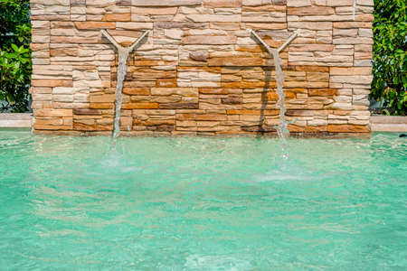 Luxury Swimming pool with a small waterfall fountain. Modern fountain detail. Waterfall drop design with decorative beige wall stone. High quality photoの写真素材