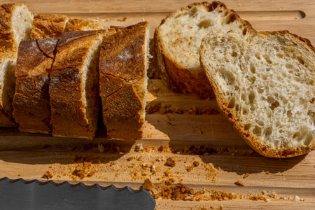 Delicious fresh baked baguette cut on a wooden cutting board with bread knife.