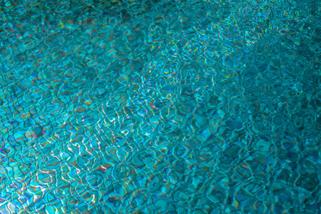 The texture of pure azure water in the swimming pool surface with ripples and sunlight reflection....