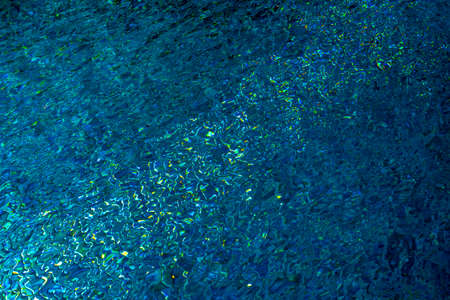 The texture of pure azure water in the swimming pool surface with ripples and sunlight reflection....