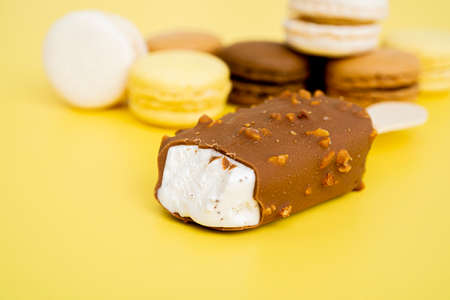 Vanilla Ice Cream with Chocolate on a Stick on a yellow background. Blurred sweets in the...