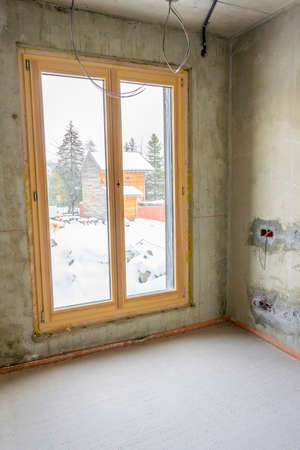 Interior of a new apartment with windows under construction without finishing in dark tones with...