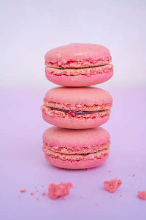 Tasty pink raspberry macaroons on light violet background. French homemade dessert with small broken pieces. High quality photoの写真素材