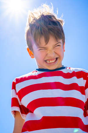 Emotional angry boy over blue sky with sun. Upset boy concept. High quality photoの写真素材