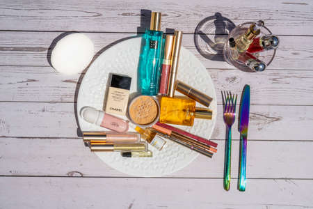 Nice, FRANCE - 21.05.2021 Aesthetic photo. Cosmetic makeup set on the plate on the table as lunch. Powder, lipstick, perfume and blush on wooden background. High quality photoのeditorial素材