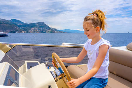 Little girl sitting at the wheel of a yacht. Sea voyage on the boat. Summer trip and vacations. childhood and happiness concept. High quality photoの写真素材