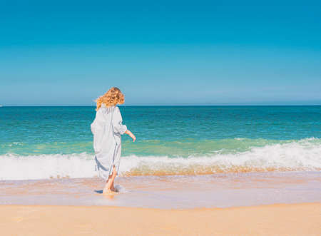 Young beautiful girl in blue dress running on the the sandy beach near the waves. High quality photoの写真素材