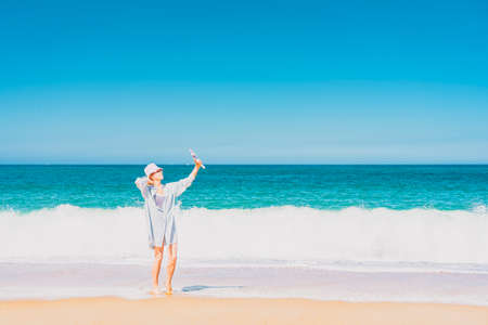 Young woman with hat standing near the sea and making selfie. Sea and sky background. Vacation and traveling concept. High quality photoの写真素材
