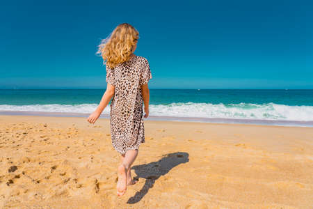 Young beautiful girl in beige dress running on the the sandy beach near the waves. High quality photoの写真素材