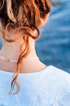 Back view of caucasian girl with long wavy hair, wearing white dress and walking in the sea water....