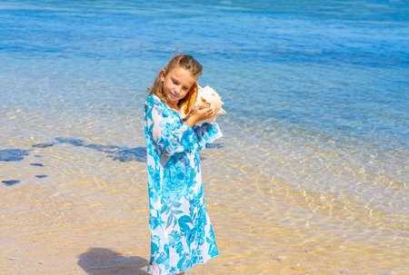 A girl holding and hearing huge big seashell near ear on the summer tropical beach. High quality...
