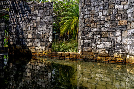 Old stone wall in the hotel with palm leaf in garden. Beautiful reflection in the water. Picture captured in the sunny morning. Mauritius island. High quality photo.の写真素材