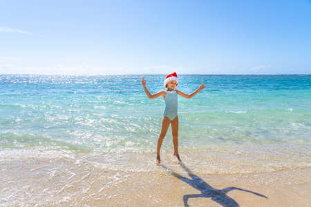Beautiful happy girl in a Christmas hat jumping in the water on the tropical summer beach. Winter holiday on a tropical island concept. High quality photoの写真素材