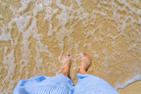 Beautiful female legs with a red pedicure on the tropical beach water. White sand beach. Tropical holidays concept. High quality photoの写真素材