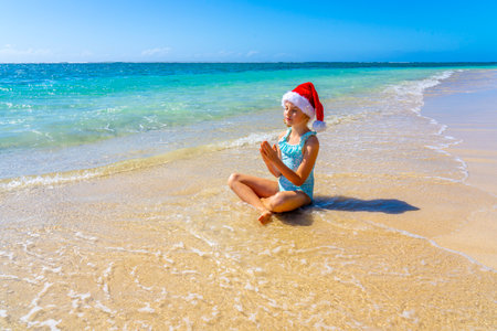 Beautiful girl in a Christmas hat meditating on the tropical summer beach. Winter holiday on a tropical island concept. High quality photoの写真素材