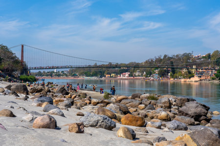 Rishikesh, Uttarakhand, India - 29.03.2023: Beautiful River Ganga in Rishikesh with people on the beach. Famouse Lakshman Jhoola bridge. Pure natural clean river water. High quality photoのeditorial素材