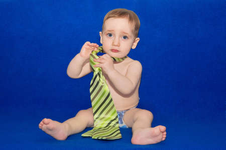 Cute Caucasian baby wearing a green tie and diaper on blue backgroundの写真素材
