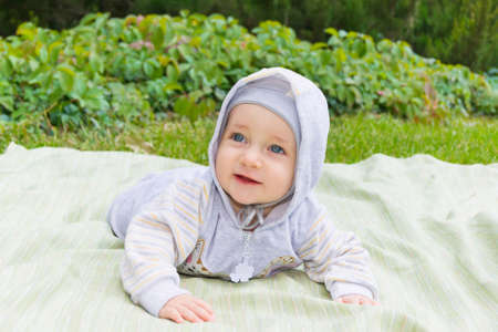 Happy child lies on a coverlet on the green grass in the park 
