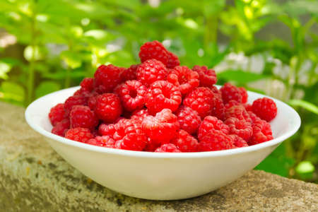 White ceramic plate up to the top filled with berries ripe raspberry lies on a stone slab