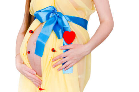 Close up belly of pregnant woman in the yellow fabric with a blue bow near the heart and ladybirds at white backgroundの写真素材