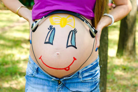 On the abdomen of a pregnant woman painted smiling face of her unborn daughterの写真素材