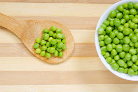 Wooden spoon and bowl with seeds of green peas on the kitchen tableの写真素材
