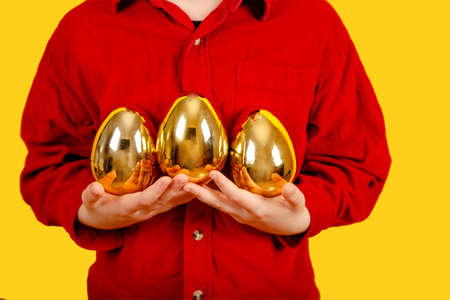 Amazing boy in bunny ears headband holding Golden Easter eggs on color background